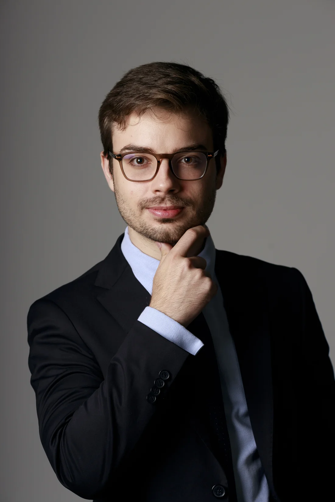 Dr. Caíque Dias in a gray suit and glasses, smiling