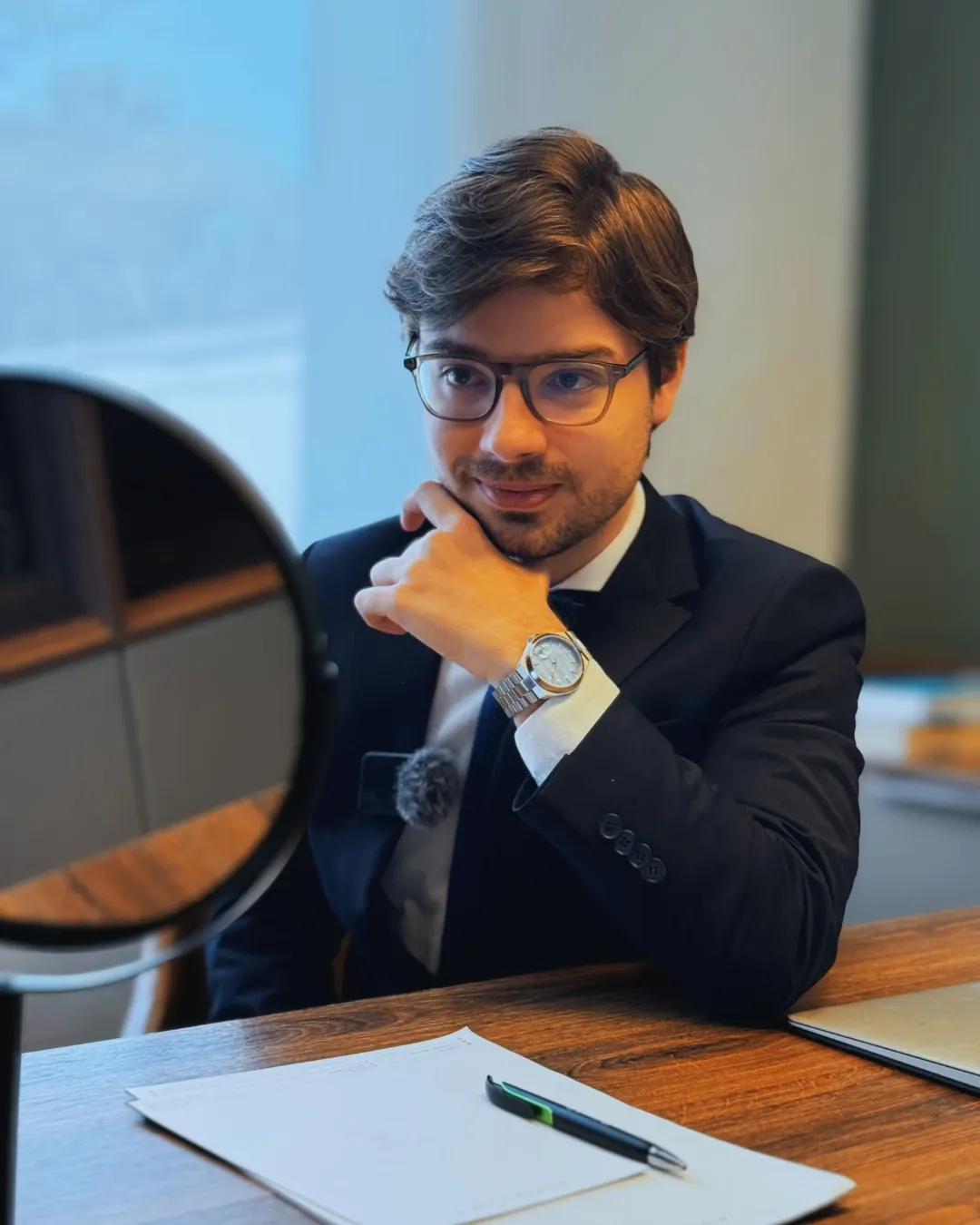 Dr. Caíque Dias seated at his office desk, next to a round mirror